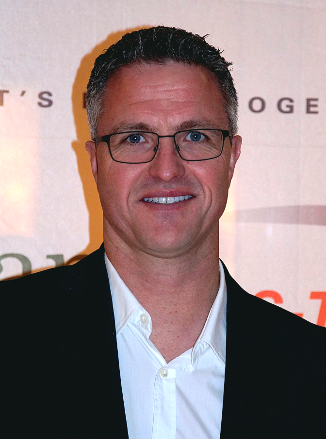 Ralf Schumacher in Hemd und Sakko vor einer Logowand
