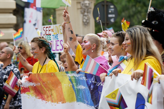 Menschen tragen Banner und Flaggen in Regenbogenfarben und laufen bei einer Parade mit.