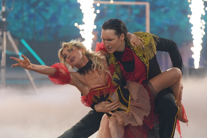 Anna-Carina Woitschack und Evgeny Vinokurov tanzen in glitzernden rot-schwarzen Kostümen, er hebt sie, sie streckt einen Arm gerade nach oben.