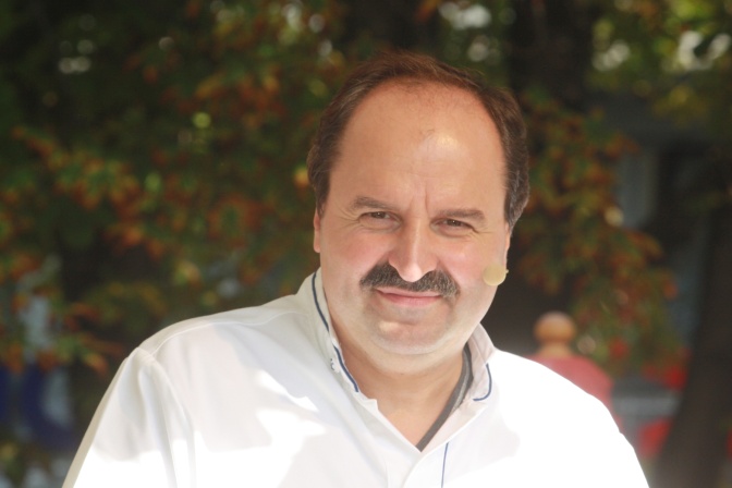 Johann Lafer in einer weißen Kochjacke mit Stirnglatze und einem Mikroheadset