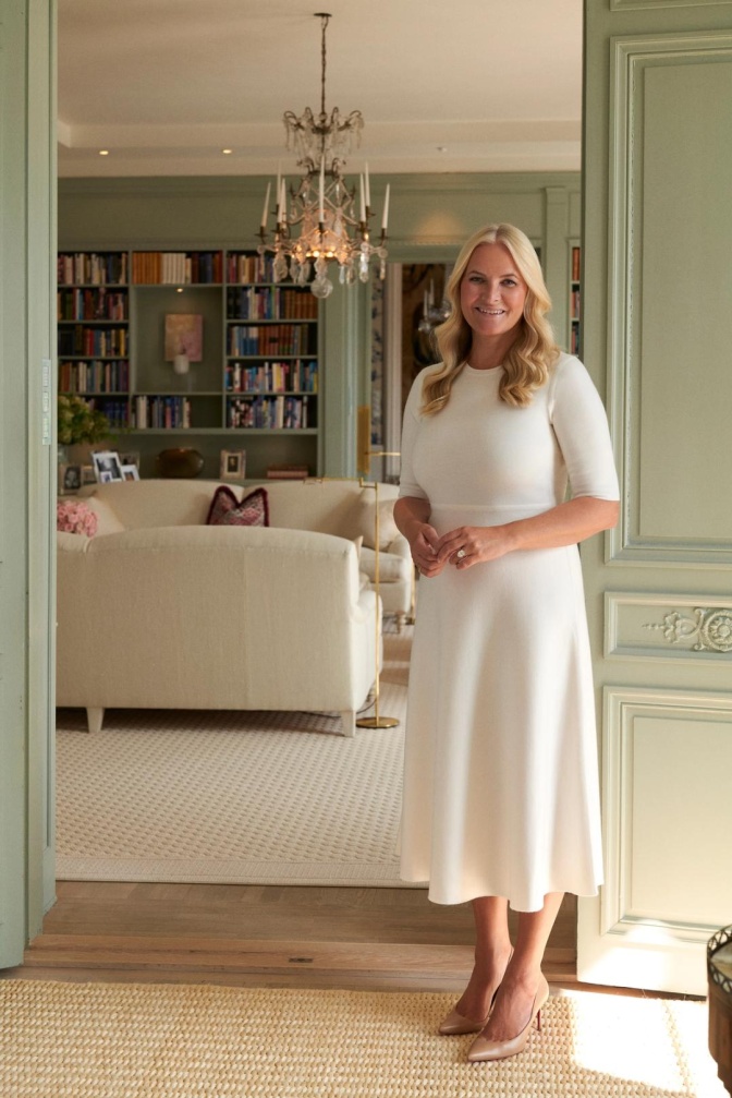 Kronprinzessin Mette-Marit in einem cremefarbenen Kleid. Sie steht in einem Wohnraum des Palasts.