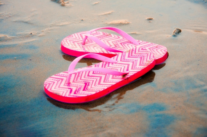 Gemusterte, pinkfarbene Flip Flops am Strand.