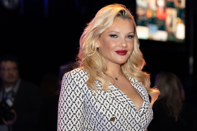 Evelyn Burdecki mit blonden in Wellen gelegten Haaren und starkem Make up. Sie trägt einen schwarz-weiß gemusterten Blazer.