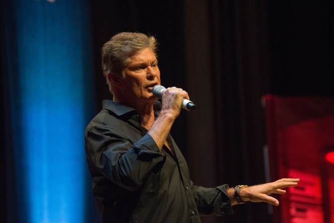 David Hasselhoff spricht auf der Bühne in ein Mikro. Die Bühne ist in blau und rot beleuchtet.