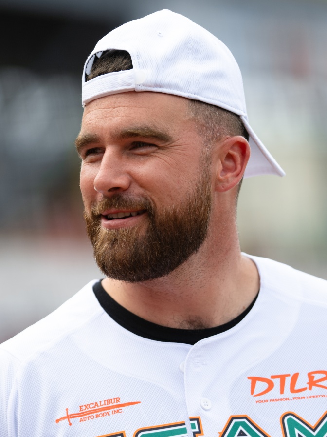 Travis Kelce mit Vollbart. Er trägt eine weiße Basecap verkehrt herum auf dem Kopf.