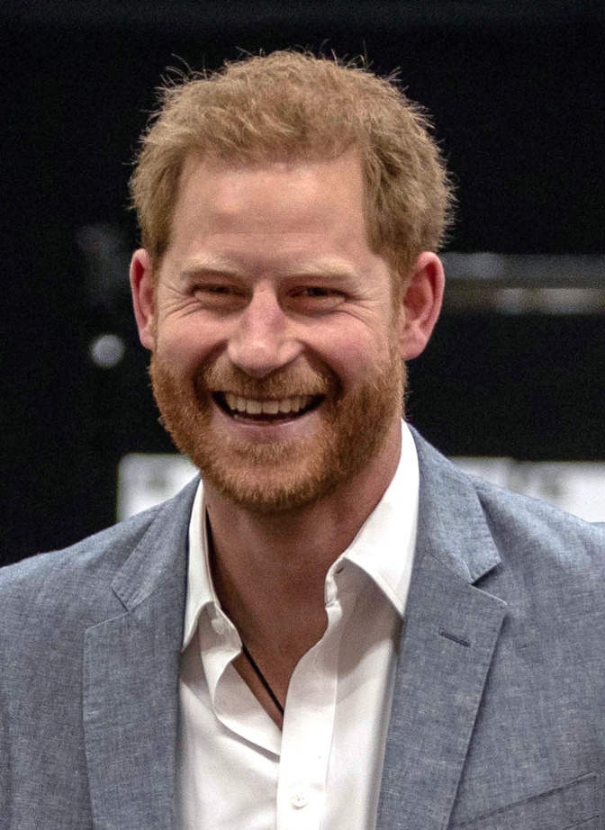 Prinz Harry in weißem Hemd und grauem Sakko. Er lacht direkt in die Kamera.
