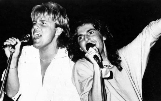 Schwarz-weiß-Foto von Dieter Bohlen und Thomas Anders aus den 1980er Jahren. Sie singen in zwei Mikrofone und lehnen sich aneinander an.