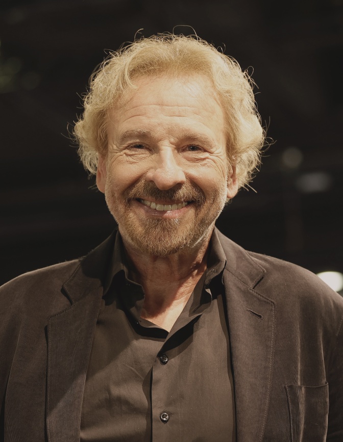 Thomas Gottschalk in schwarzer Kleidung mit kurzen, gelockten blonden Haaren. Er schaut direkt in die Kamera.