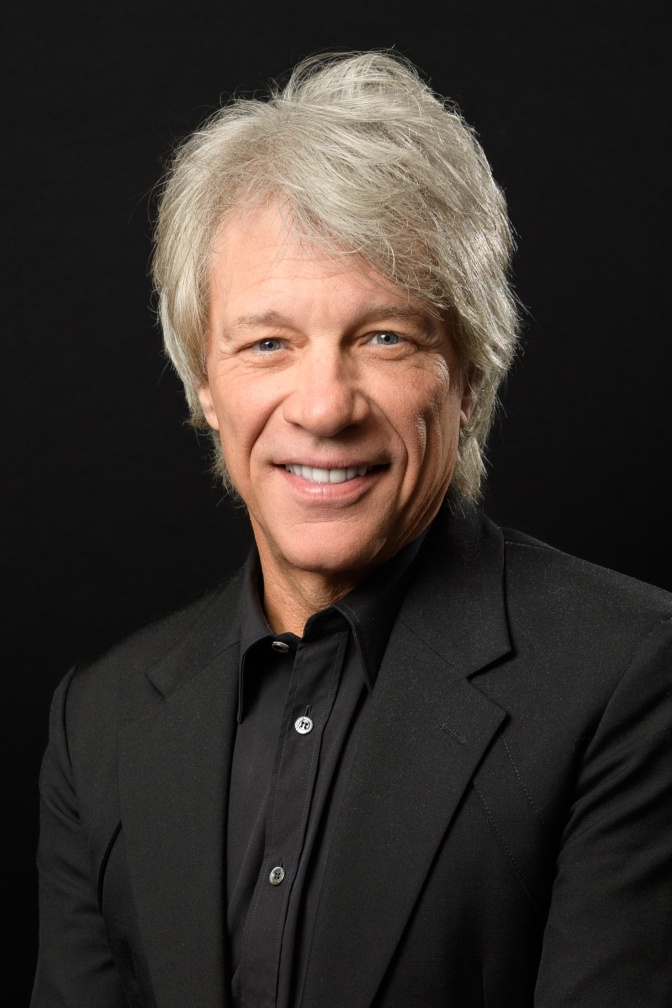 Jon Bon Jovi mit grauen Haaren in einem schwarzen Hemd. Er lächelt direkt in die Kamera.