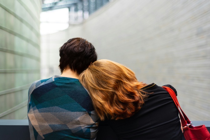 2 Personen, ein Mann und eine Frau, sitzen nebeneinander und lehnen sich aneinander an. Die beiden sind von hinten zu sehen.