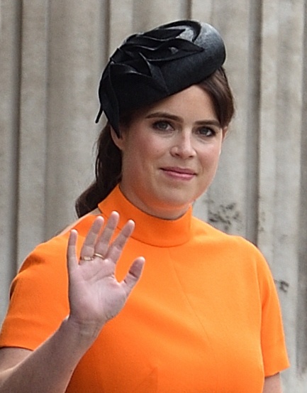 Prinzessin Eugenie in einem leuchtend orangenen Kleid mit einem kleinen schwarzen Hut. Sie winkt.