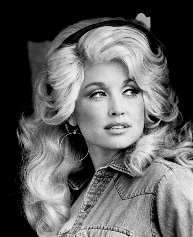 Schwarz-weiß-Foto von Dolly Parton aus den 1970er Jahren. Sie schaut mit ernstem Blick seitlich an der Kamera vorbei.