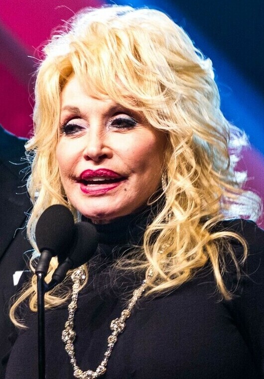 Dolly Parton mit voluminöser blonder Perücke in einem schwarzen Rollkragenpullover.