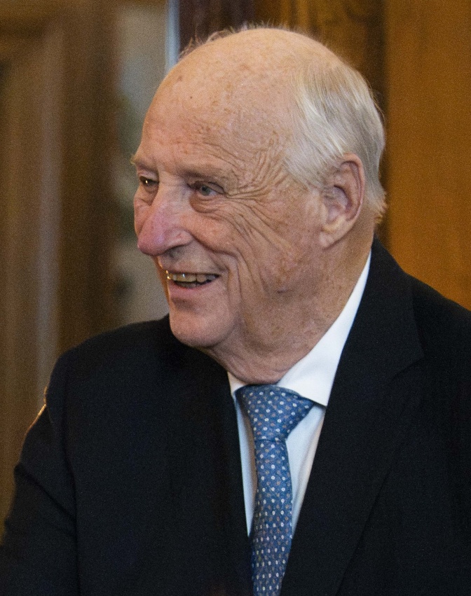 König Harald ihn einem schwarzen Anzug mit blauer Krawatte. Er hat einen dünnen Kranz weißer Haare und eine Stirnglatze.