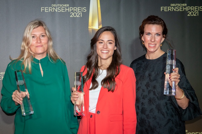 3 Frauen stehen mit Preisen in der Hand vor einer Logowand des Deutschen Fernsehpreises und lächeln breit.
