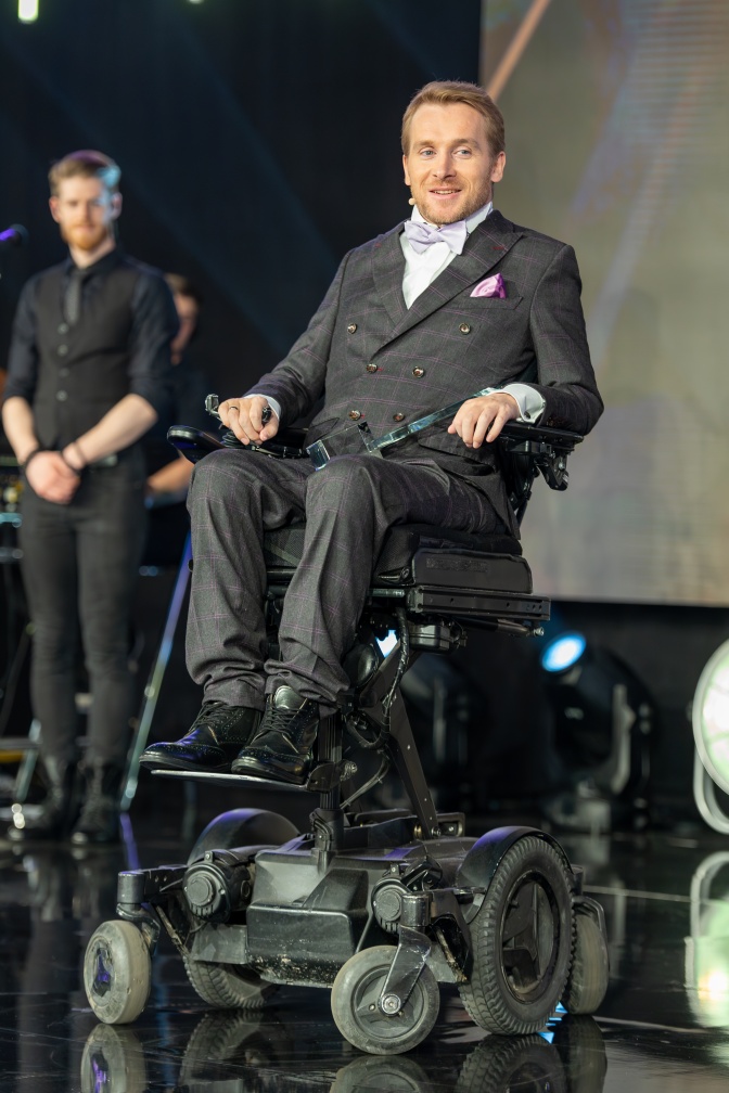 Samuel Koch in einem Rollstuhl in Anzug und weißem Hemd mit Fliege.