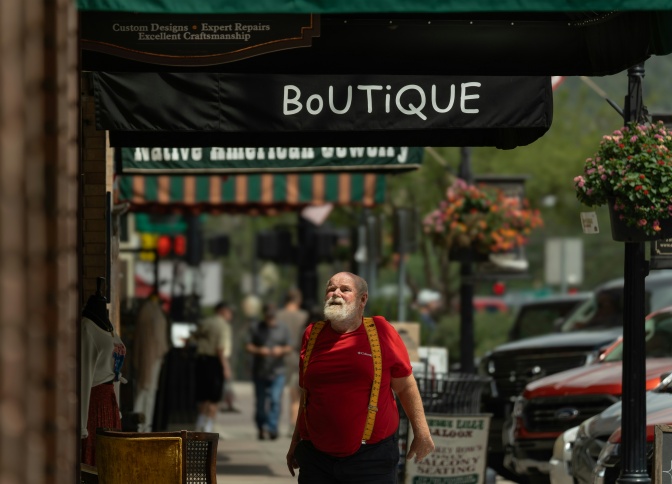 Ein älterer Mann mit weißem Bart und dickem Bauch steht auf der Straße unter einem Vordach mit der Aufschrift Boutique.