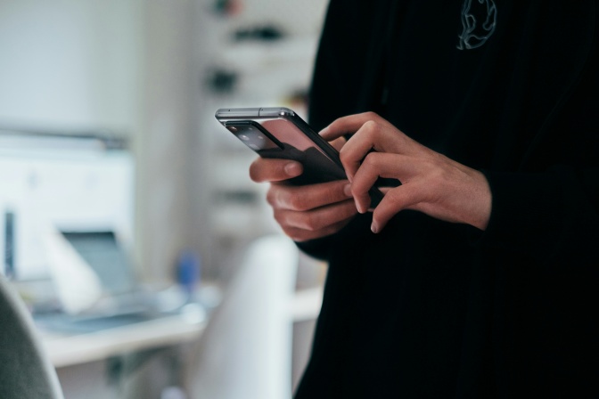 Eine Person recherchiert am Handy. Man sieht nur Oberkörper und Hände der Person.