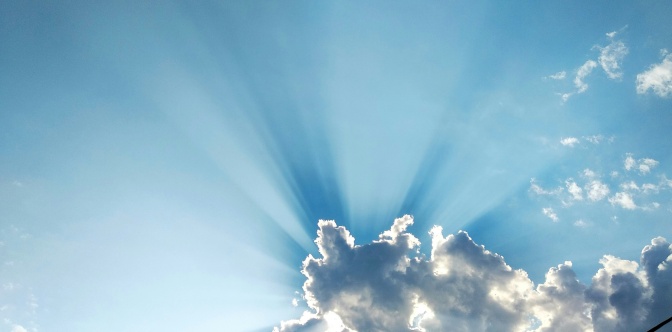 Sonnenstrahlen scheinen durch eine weiße Wolke am strahlend blauen Himmel