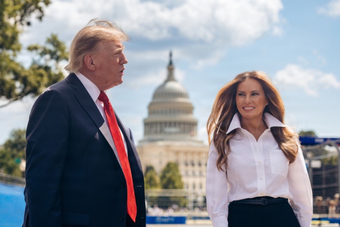 Melania und Donald Trump stehen vor dem Capitol, sie lächelt, ihre Haare wehen im Wind.