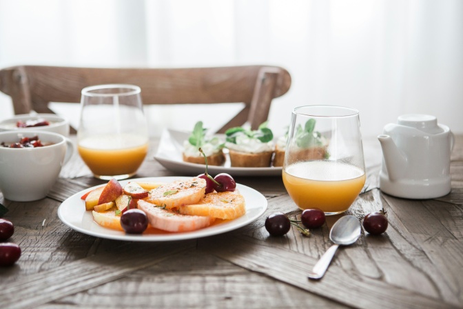 Ein Teller mit Obst und 2 Gläser Orangensaft auf einem Frühstückstisch