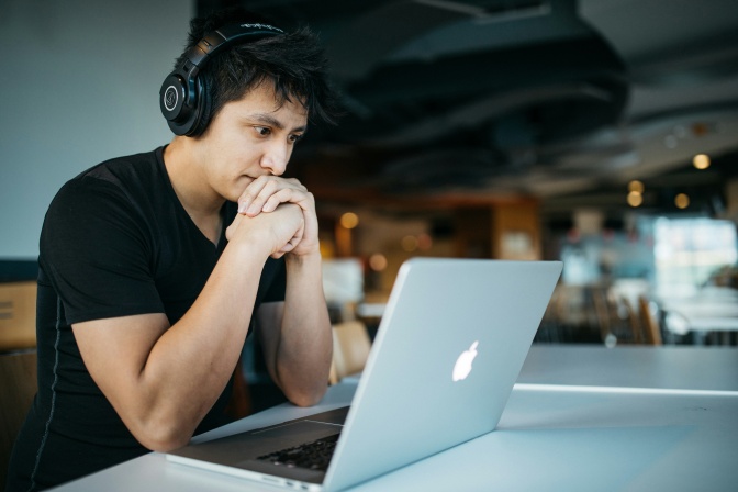Ein schwarzer Mann mit Kopfhörern schaut nachdenklich auf den Bildschirm eines Laptops.