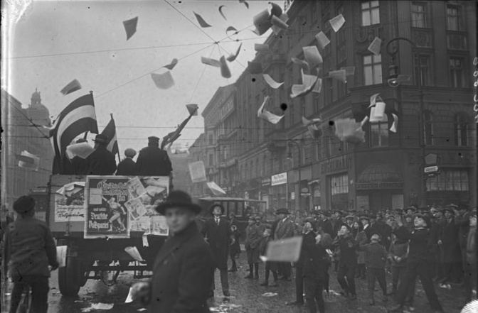 Schwarz-weiß-Fotos einer Straßenszene. Flugblätter wirbeln durch die Luft.