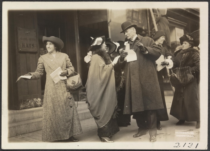 Schwarz-weiß-Foto mehrerer Frauen in Kleidung aus den 1910er Jahren, die Flugblätter an Männer verteilen.