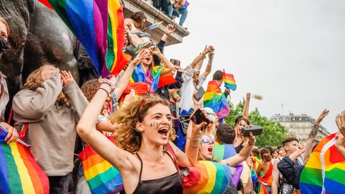 Eine Frau in einem Tanktop steht in einer Menschenmenge und schwenkt eine Regenbogenflagge.