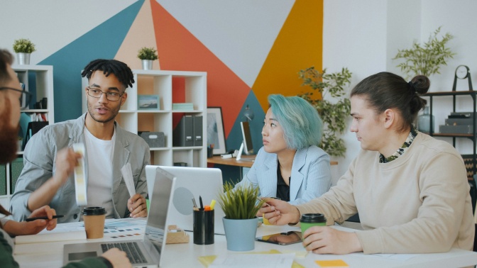Eine Gruppe diverser Menschen sitzt zusammen am Tisch und ist im Arbeitsgespräch.