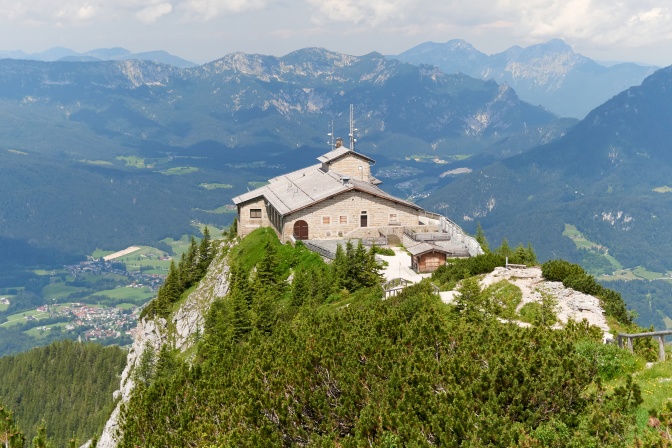 Eine Berggaststätte auf einer Bergspitze, dahinter Bergpanorama.