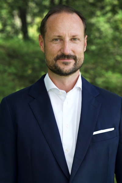 Kronprinz Haakon in einem blauen Sakko und einem weißen Hemd. Er steht im Freien und schaut genau in die Kamera.