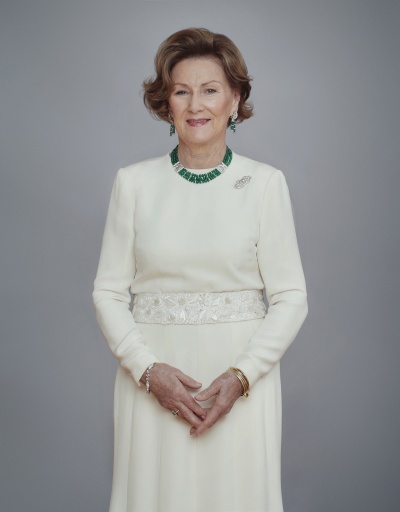 Ganzkörperfoto von Sonja von Norwegen in einem weißen Kleid. Sie steht aufrecht und hat die Hände ineinander gefaltet. Sie schaut direkt in die Kamera.