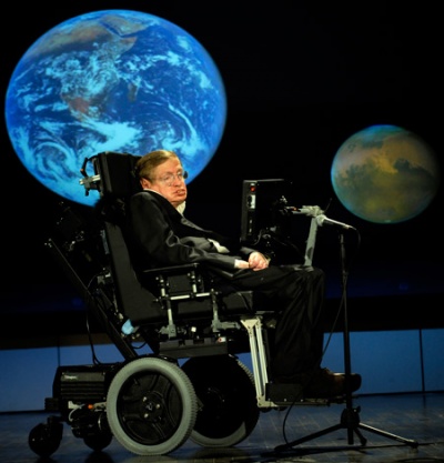 Stephen Hawking in seinem elektrischen Rollstuhl auf der Bühne, im Hintergrund eine Projektion der Weltkugel.