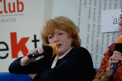 Hannelore Hoger spricht in ein Mikrophon. Im Hintergrund sind Logos verschiedener Fernsehsender zu sehen.