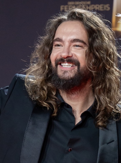 Tom Kaulitz mit braunen langen Haaren und Vollbart. Er lächelt breit.