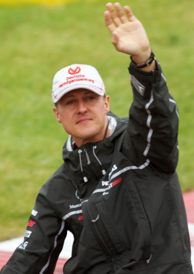 Michael Schumacher trägt eine weiße Schirmmütze. Er hebt die Hand und winkt.