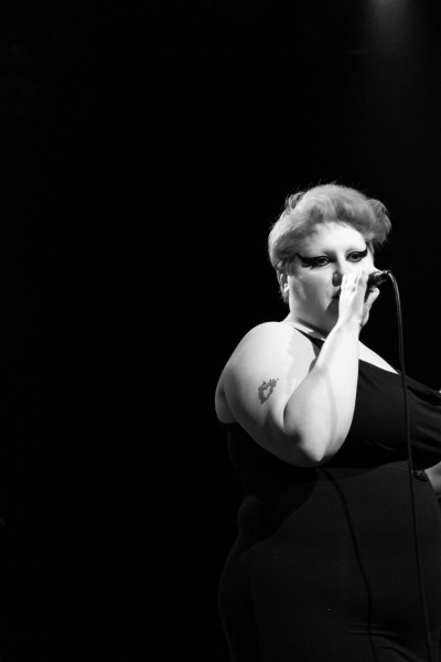Ein schwarz-weiß-Foto von Beth Ditto auf der Bühne. Sie singt in ein Mikrophon.