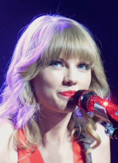 Taylor Swift mit blonden Haaren und Pony. Sie singt in ein Mikrophon.