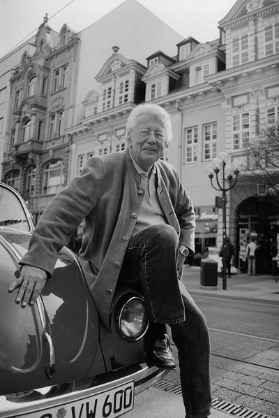 Ein schwarz-weiß-Bild von Dieter Thomas Heck, der an der Kühlerhaube eines VW Käfer lehnt.