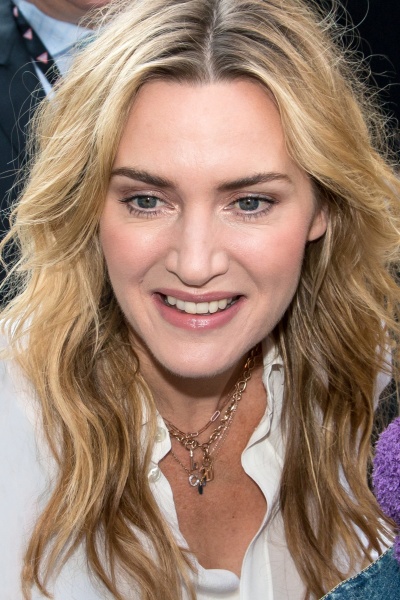 Kate Winslet mit blonden, in Wellen gelegten Haaren. Sie trägt eine weiße Bluse und ist leicht von oben fotografiert.