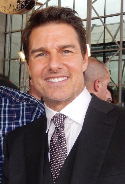 Tom Cruise in Anzug und Krawatte. Er hat einen Drei-Tage-Bart und lächelt.