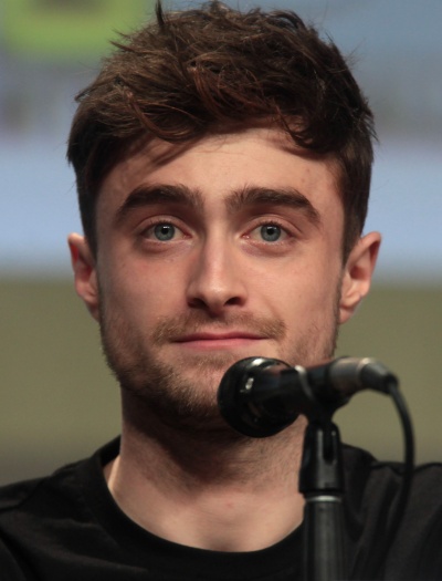 Daniel Radcliffe mit kurzen. zur Seite frisierten Haaren. Er spricht in ein Mikrophon.