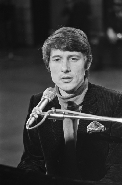 Ein schwarz-weiß-Foto von Udo Jürgens am Klavier. Er singt in ein Mikrophon und trägt Anzug und Krawatte.