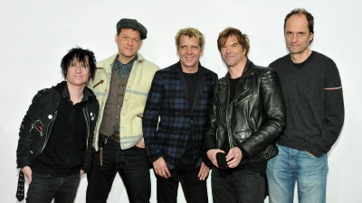 Die 5 Bandmitglieder stehen nebeneinander vor einer weißen Wand.