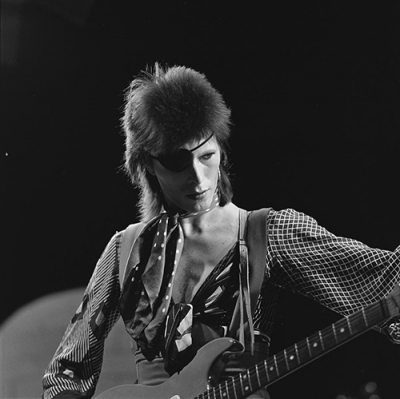 Ein schwarz-weiß-Foto von David Bowie auf der Bühne. Er trägt eine Augenklappe und hat eine Vokuhila-Frisur.