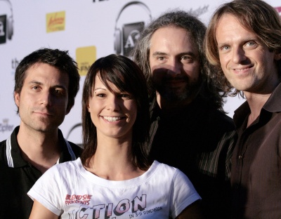 Christina Stürmer steht mit 3 Musikern ihrer Band vor einer Logowand. Sie trägt ein weißes T-Shirt und lächelt.