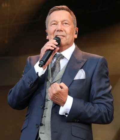 Roland Kaiser in Anzug und Krawatte. Er singt in ein Handmikro.