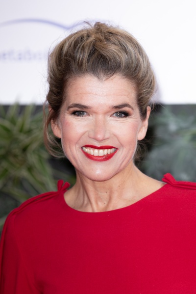 Anke Engelke mit hochgesteckten Haaren in einem leuchtend roten Oberteil und passendem Lippenstift.