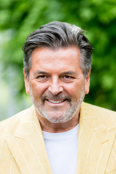 Thomas Anders mit grauem Vollbart. Er trägt ein hellgelbes Sakko und schaut lächelnd in die Kamera.